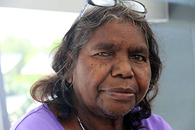Close-up face of Irene Nangala, a shrewd-looking Aboriginal woman with reading glasses on her head