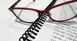 Red-rimmed glasses sitting on a binder showing a schedule of times