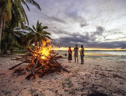 Bon fire on beach with three people standing around it