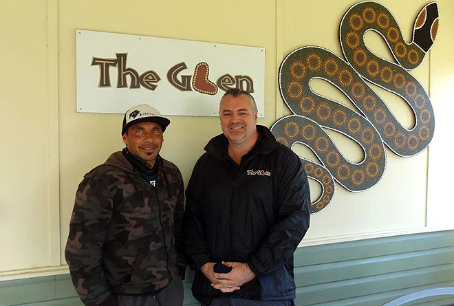 Two men standing in front of a sign for 'The Glen' and a large decorative snake