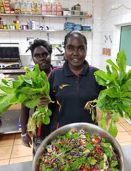 Two young Yolngu women in a shop, one holding salad greens, in front of a large bowl of salad