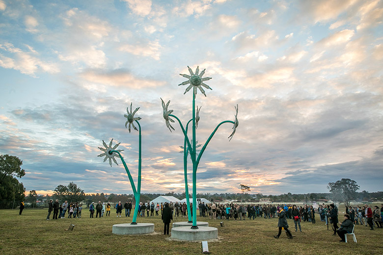 Giant woven flannel flowers in a field with a large crowd of people