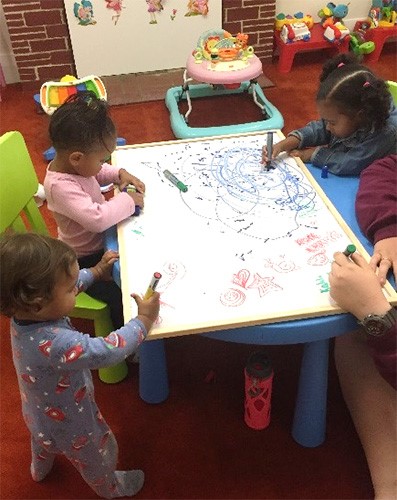 young children standing around and drawing on a flat whiteboard