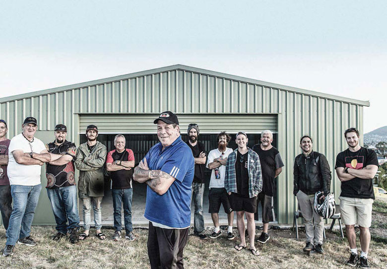 Aboriginal men standing happily in front of a large shed—Tasmania's first men's shed