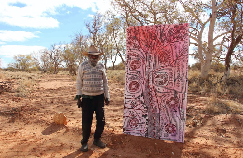 Peter Mungkuri standing next to a large pink and black painting at Iwantja, 2020