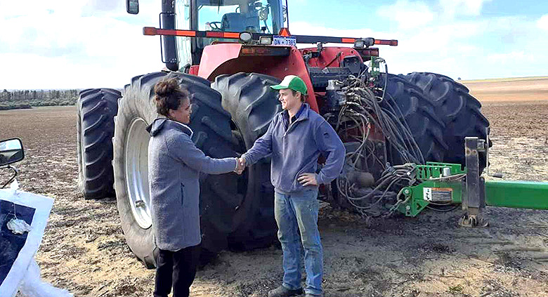 Aboriginal woman shaking hands with a white man in front of a tractor