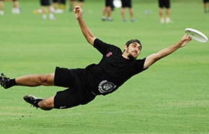 Man in black diving for a frisbee on a grass playing field