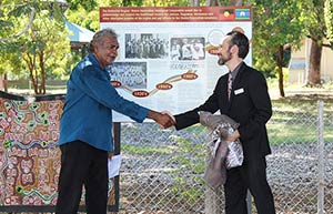 two men shake hands in front of signage about a garden