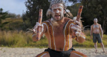 Gumbaynggir man dressed for ceremony, holding clapsticks, facing the camera