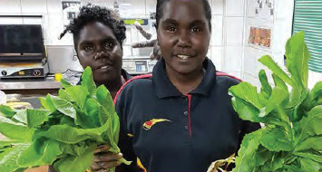 Two young Yolngu women in a shop, one holding salad greens, in front of a large bowl of salad