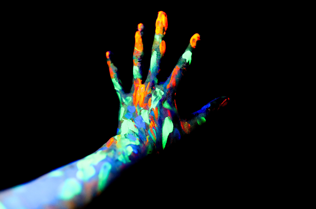 A hand and forearm covered in many colours of paint on a black background