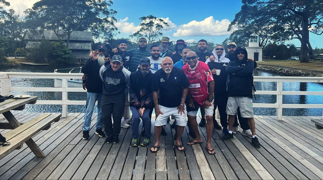 A group of men stands on a deck with water behind them