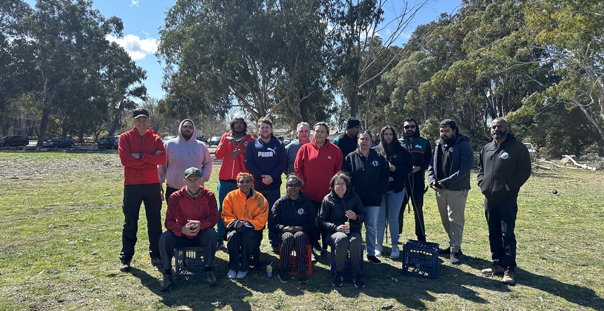 A group of people in two rows stands on grass with trees behind them