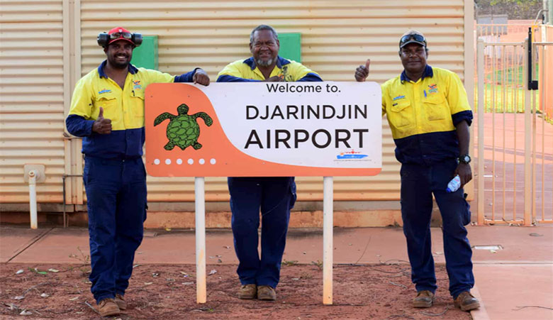 3 Aboriginal men standing happily in front of a sign with a turtle and the words 'Welcome to Djarindjin Airport'
