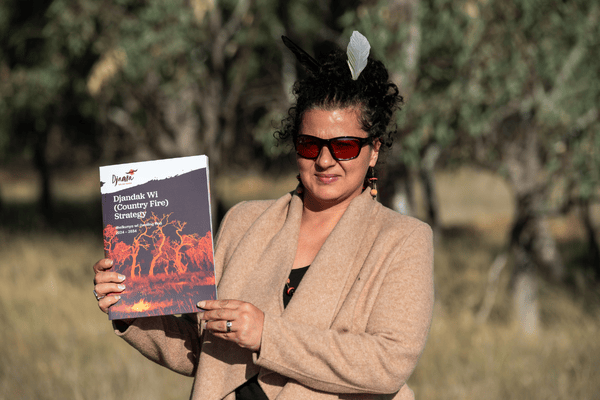 A woman stands outdoors holding a book