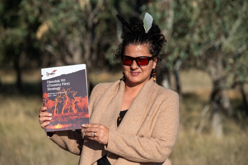 A woman stands outdoors holding a book