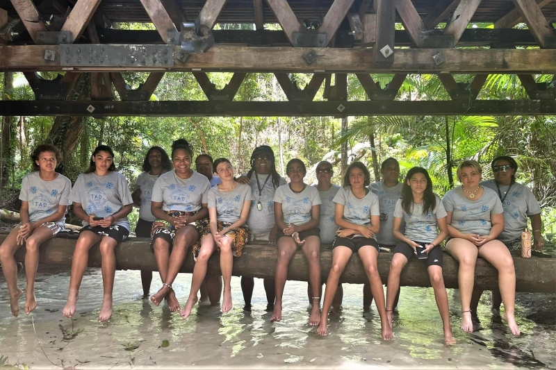 A group of girls sit on the bottom supports of a bridge with their feet dangling in water