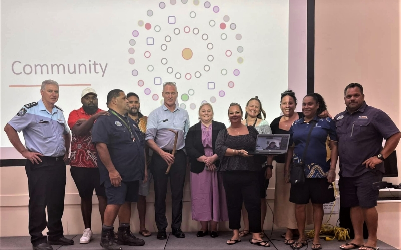 A group of people stands on a stage. A screen behind them reads Community