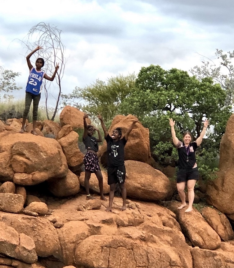 Four young people stand on rocks with their hands in the air