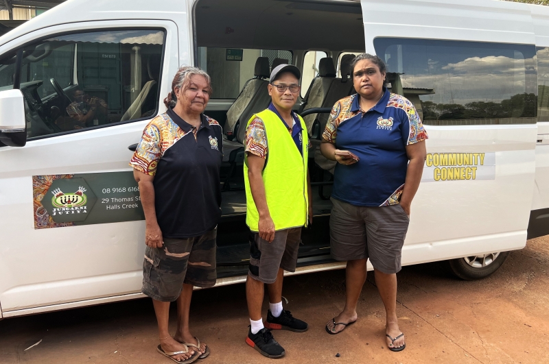 Three people stand in front of a white van