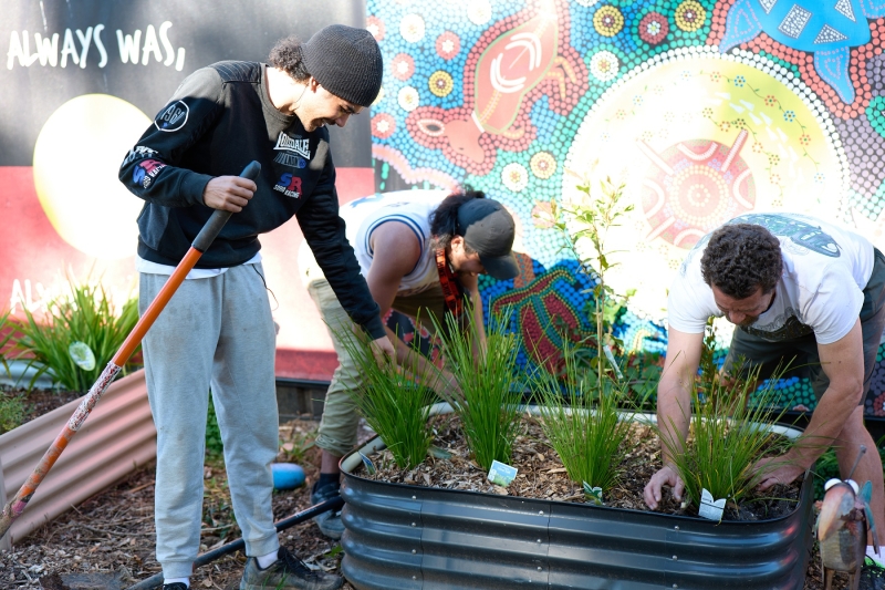 Three people work on a raised garden bed