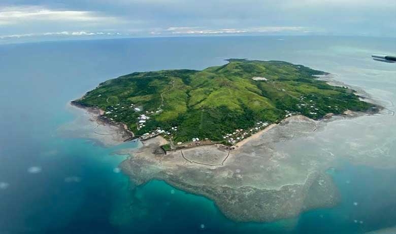 A green island surrounded by a rocky underwater shelf and blue sea