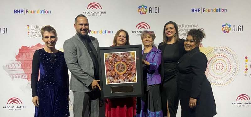 A group of people hold a large rectangular award