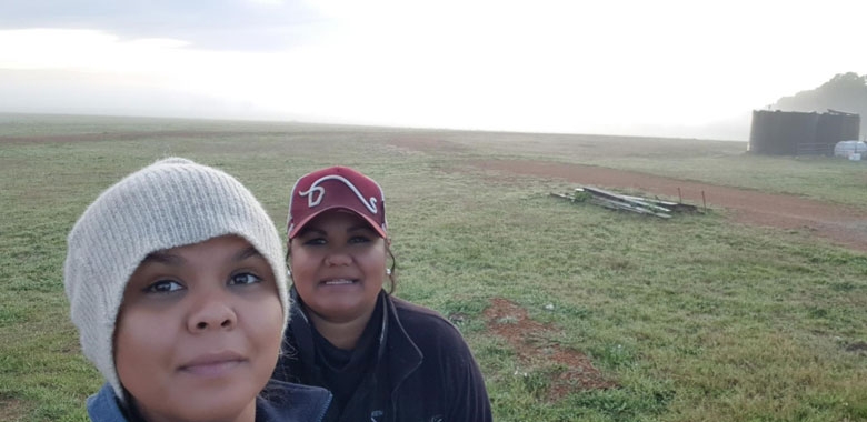 Two young women smile at the camera in a large, misty paddock