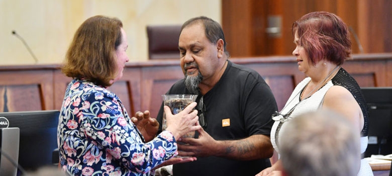 Two people pass a small urn to a 3rd person in a courtroom