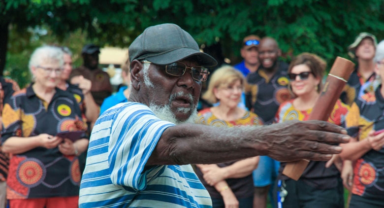 A man gestures to the right of the camera. A crowd is in the background