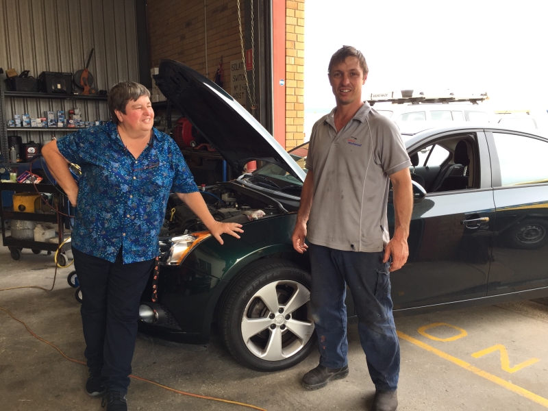 Woman and a man stand happily in front of a car in a mechanic workshop