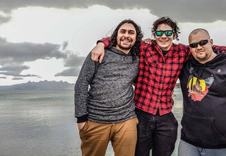 Three men with their arms around each other pose for the camera