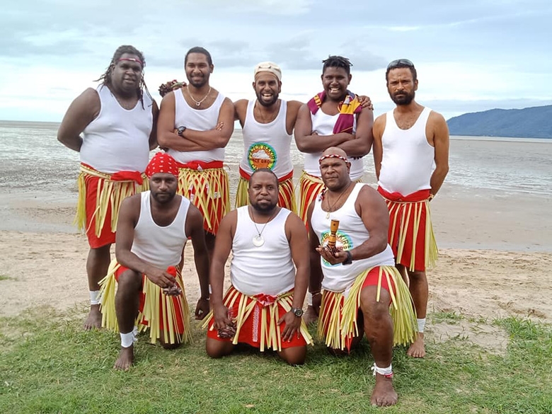 A group of people all dressed in a white singlet and mock grass skirtposes on a beach
